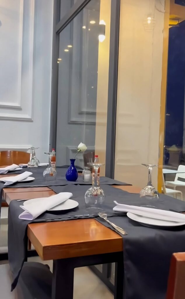 Elegant Dining Space My Octopus Dakhla A neatly set dining table inside My Octopus Dakhla with white plates, folded napkins, upside-down wine glasses, and a blue vase holding a white flower near a window.